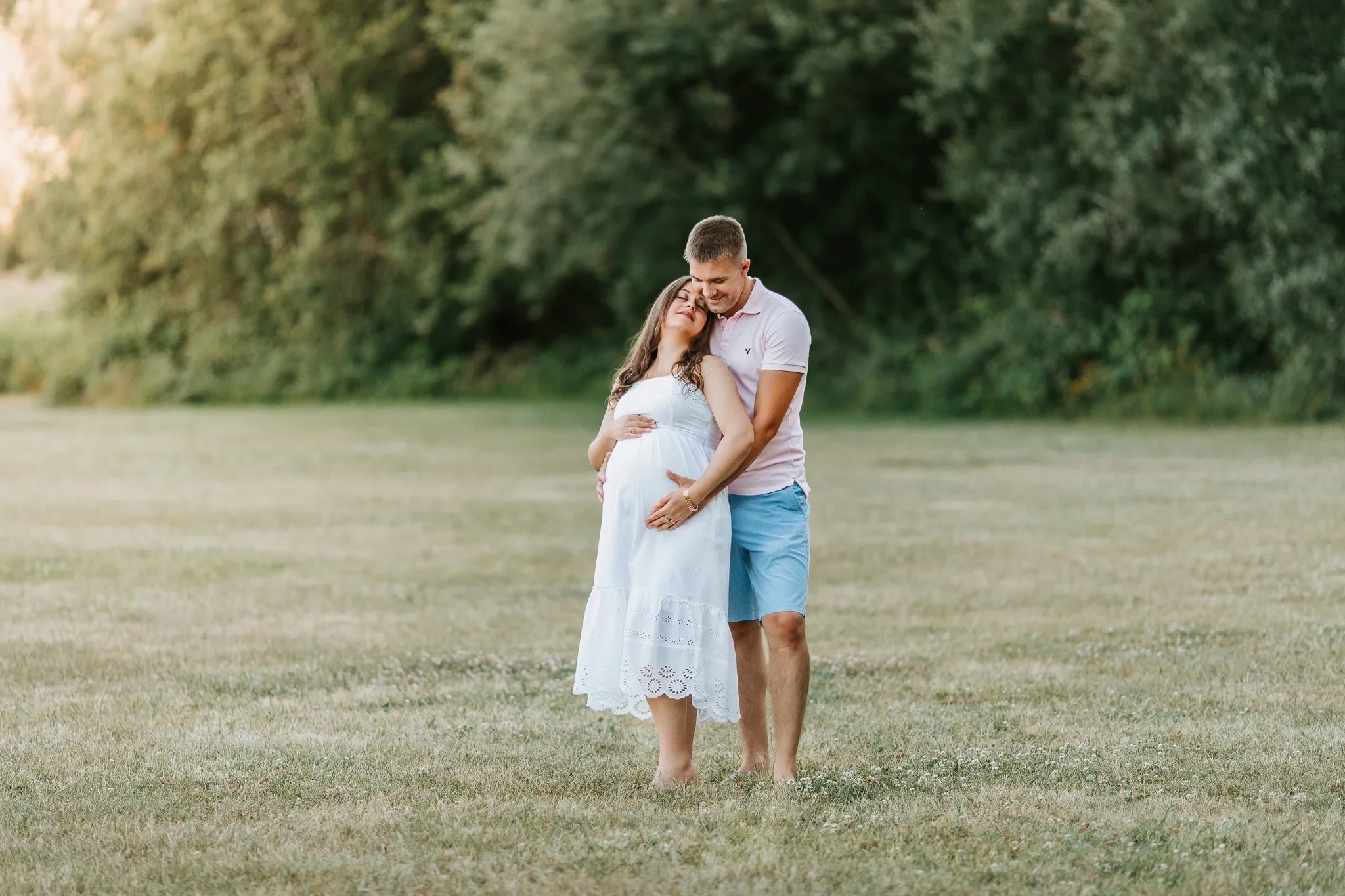 Two adults embrace in a grassy clearing with trees behind them