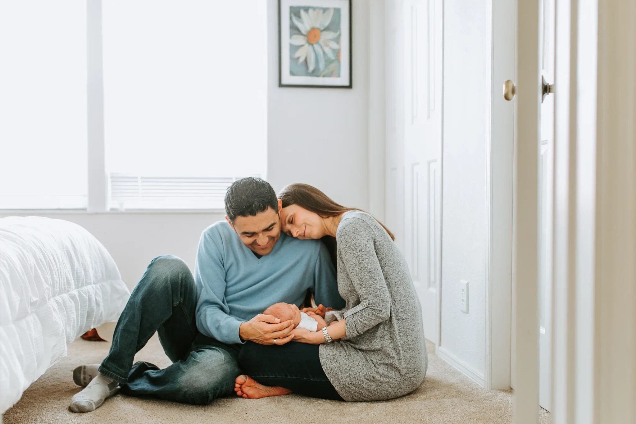 Two adults sit on the bedroom floor holding a baby
