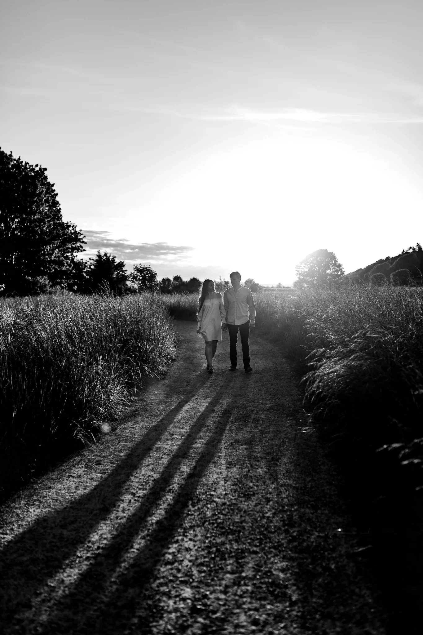 Black-and-white view of two people walking toward sunlight through tall grass