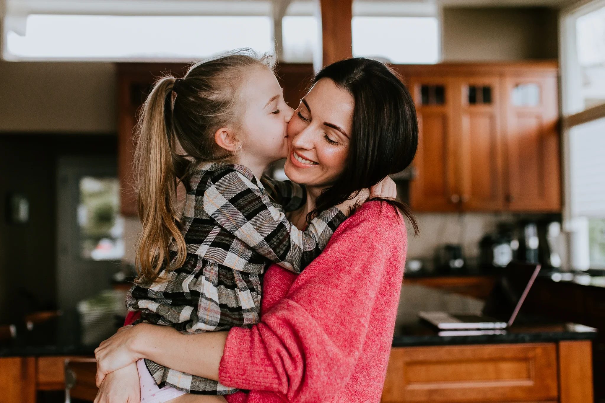 Child kisses a woman on the cheek in a kitchen
