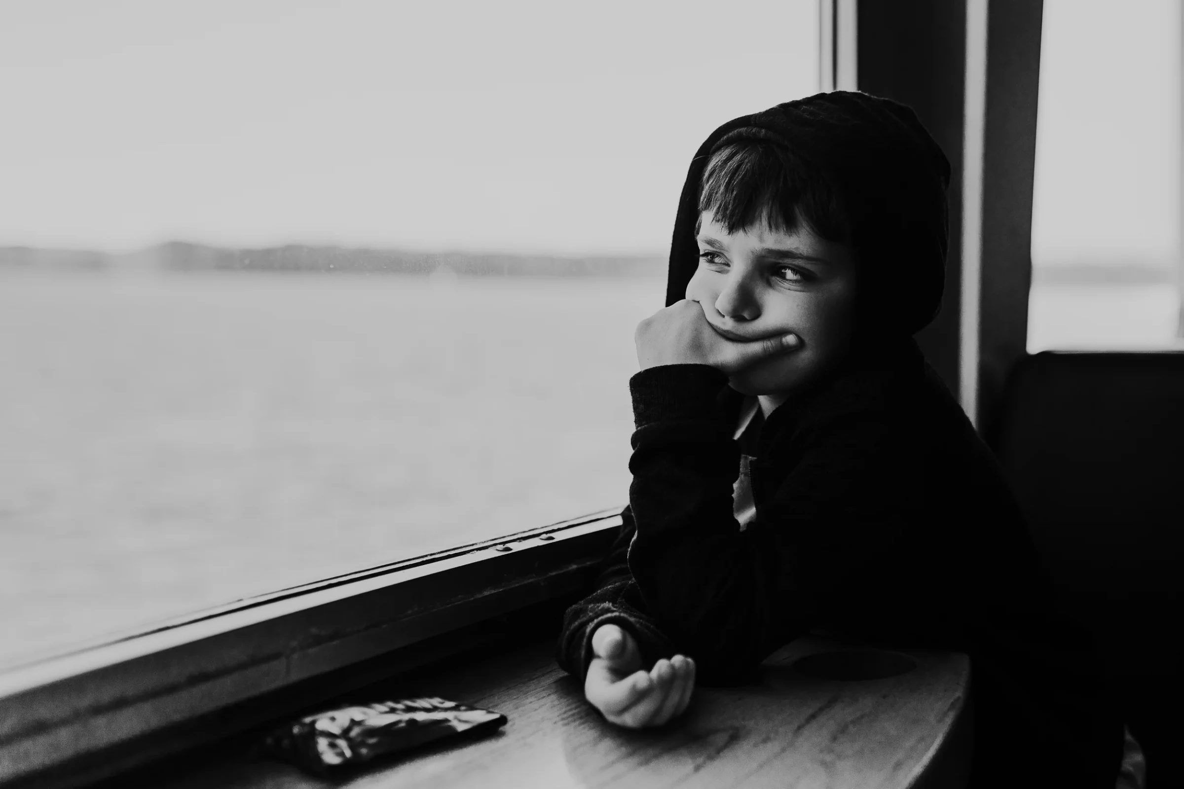 Black-and-white portrait of a child looking through a window with chin resting on one hand