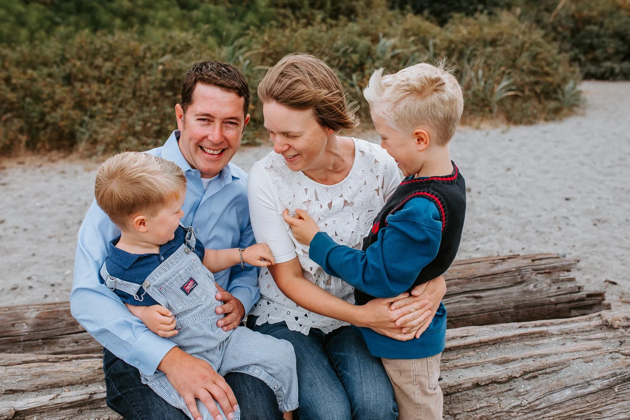 Family of four sits together on driftwood at the beach