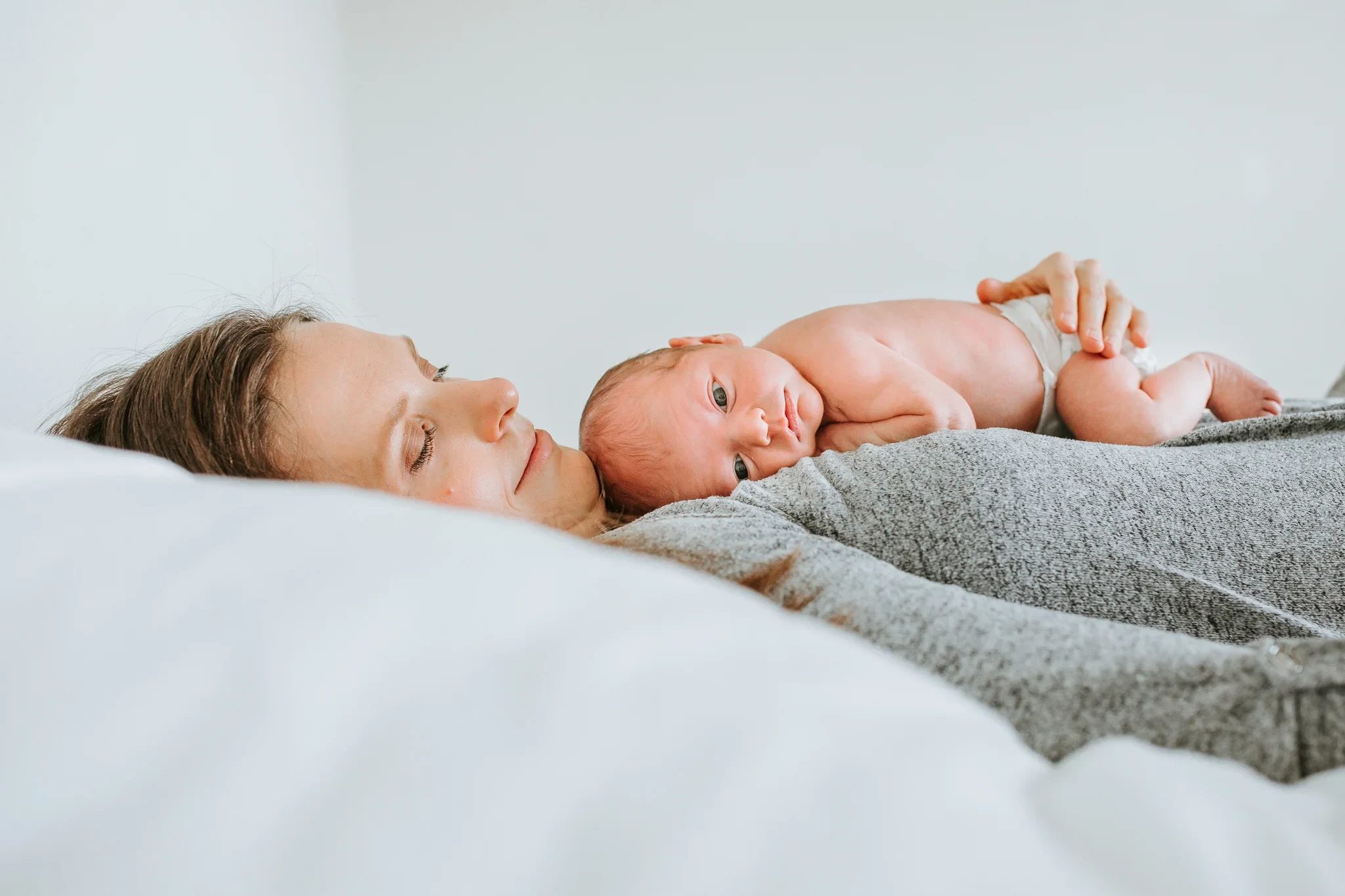 Baby rests on a reclining woman’s chest on a white bed