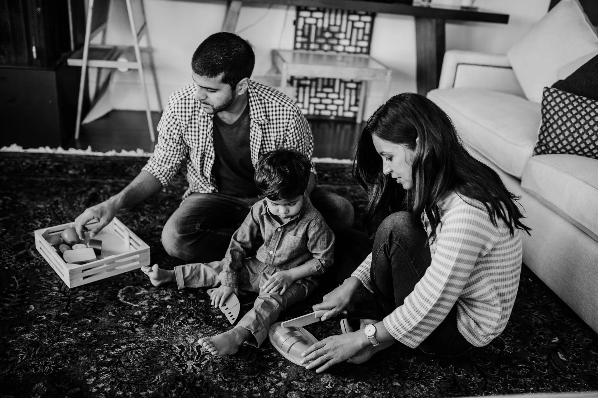 Black-and-white photograph of a family looking at books on a living-room rug