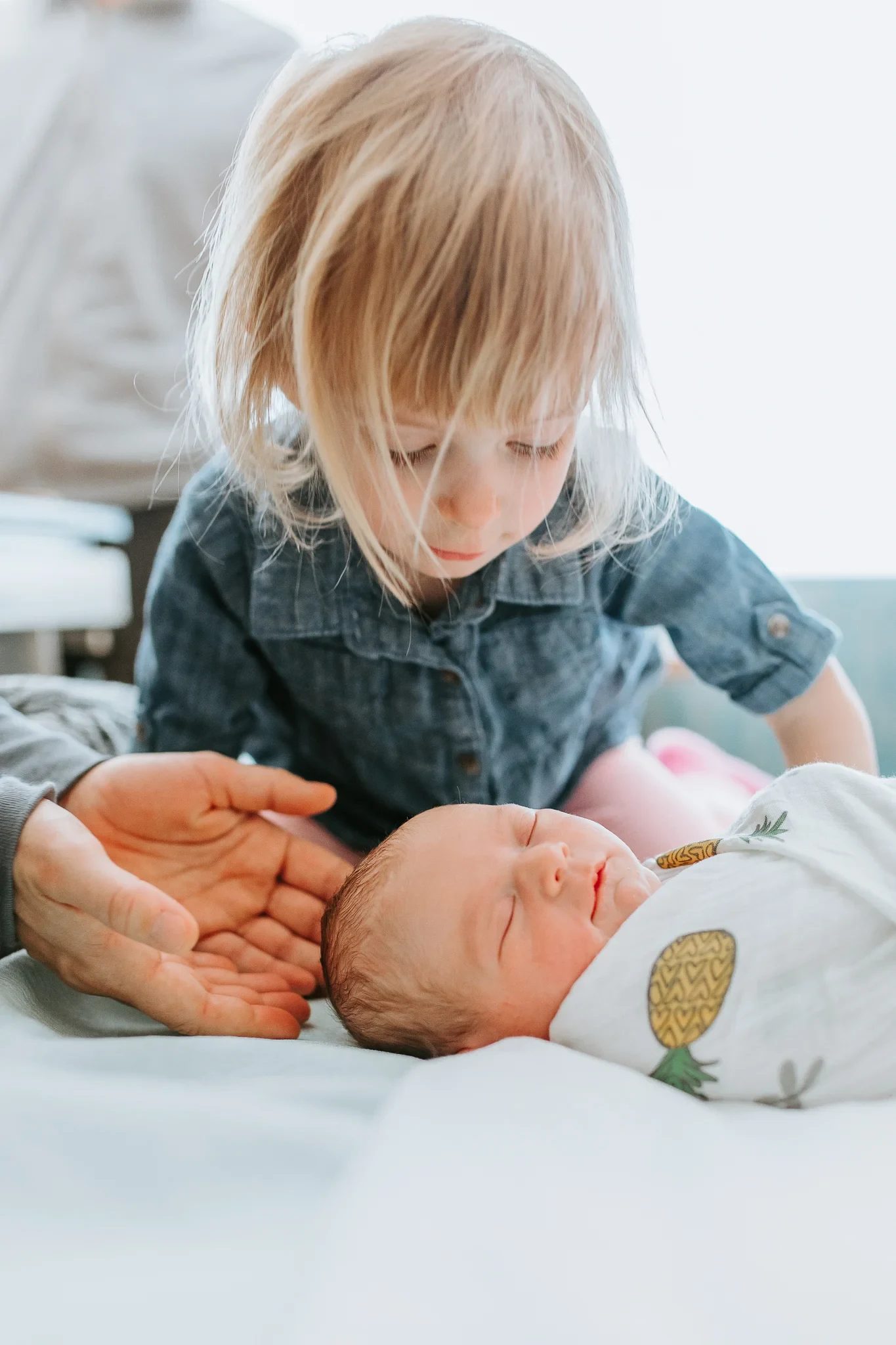 Child bends close to a baby lying on a bed