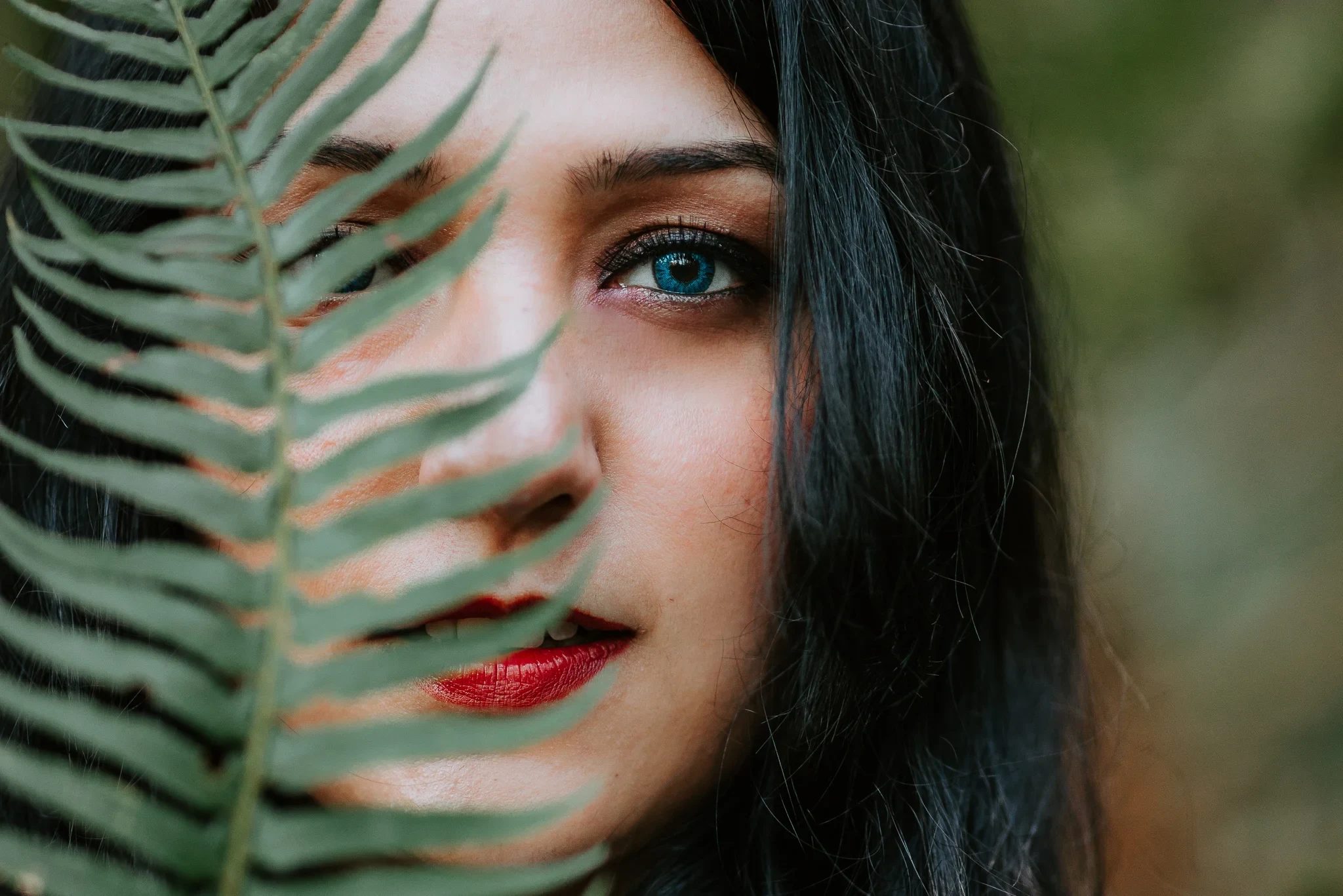 Close-up portrait of a woman’s face partly hidden behind a fern