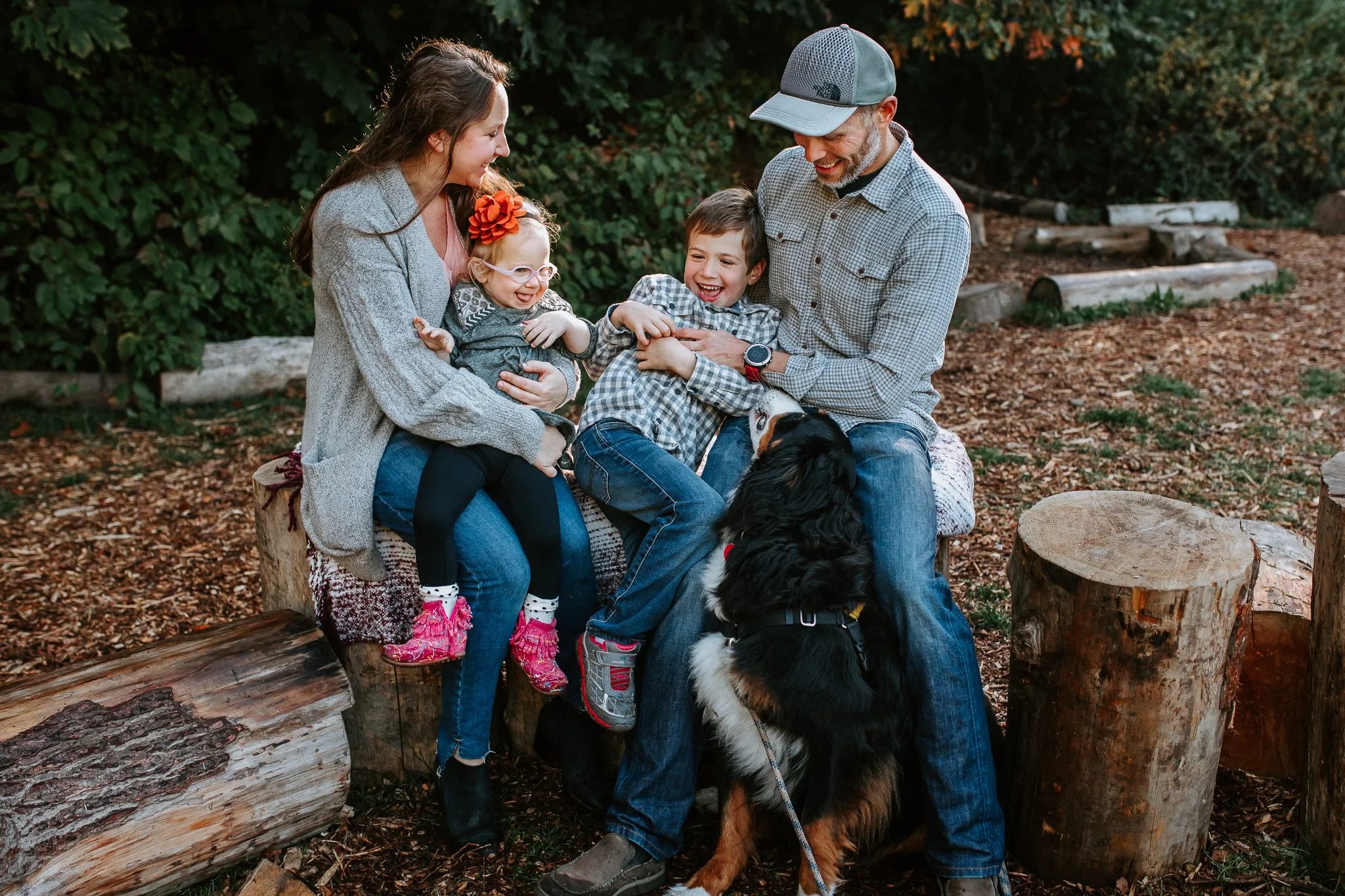 Two adults and two children sit on a fallen tree in the woods