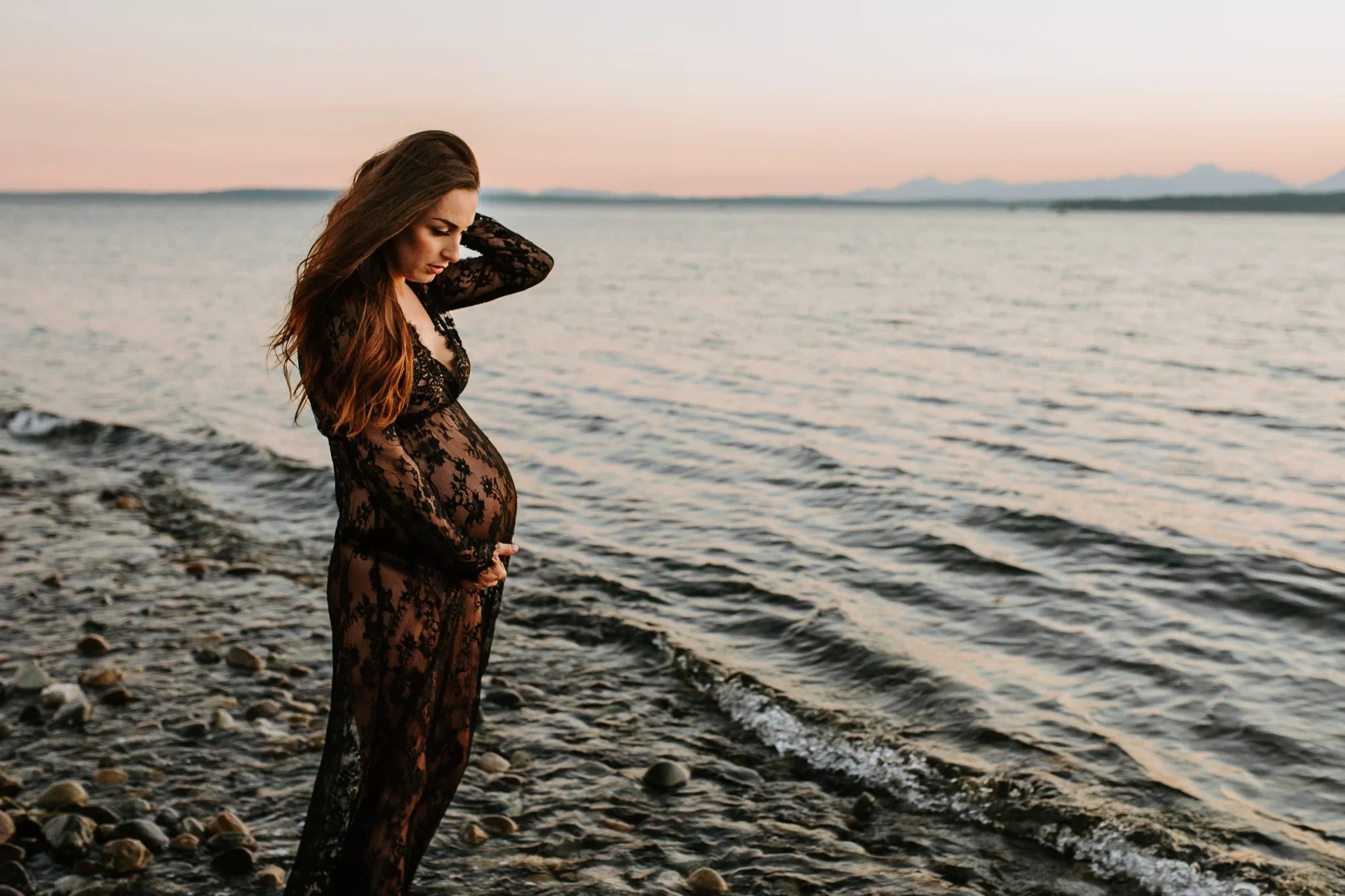 Woman in black lace stands beside the shoreline at dusk