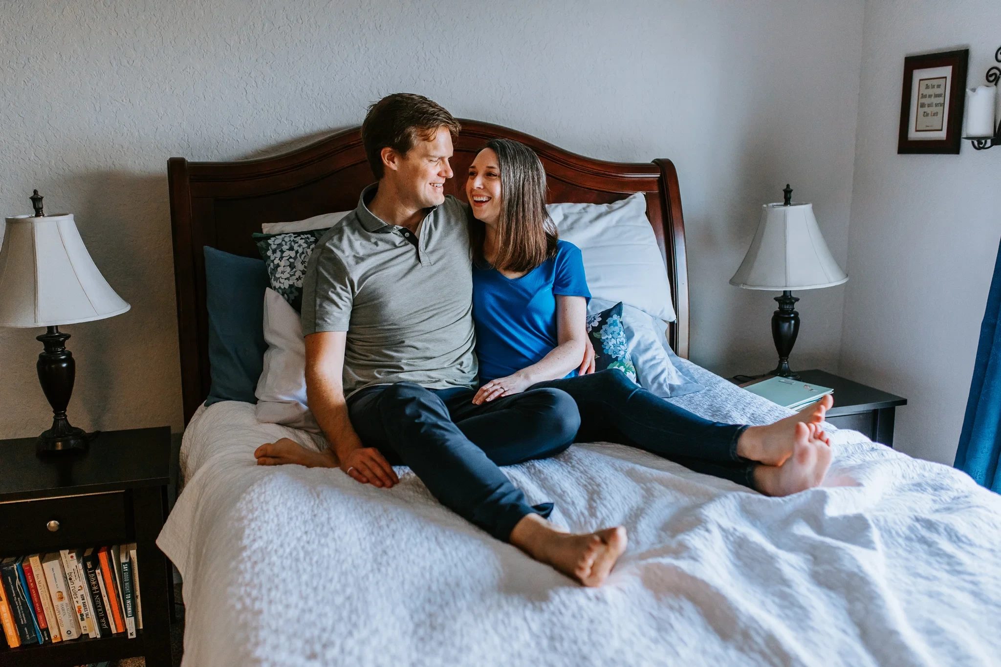 Two adults sit together on a bed in a bright bedroom