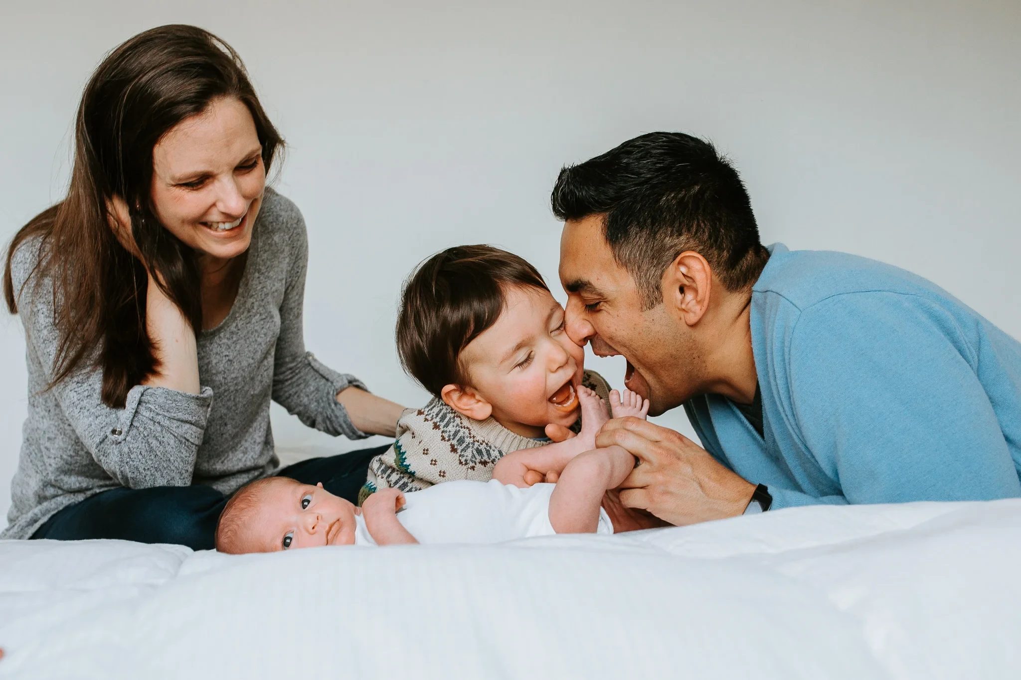Two adults smile beside a child and baby on a bed
