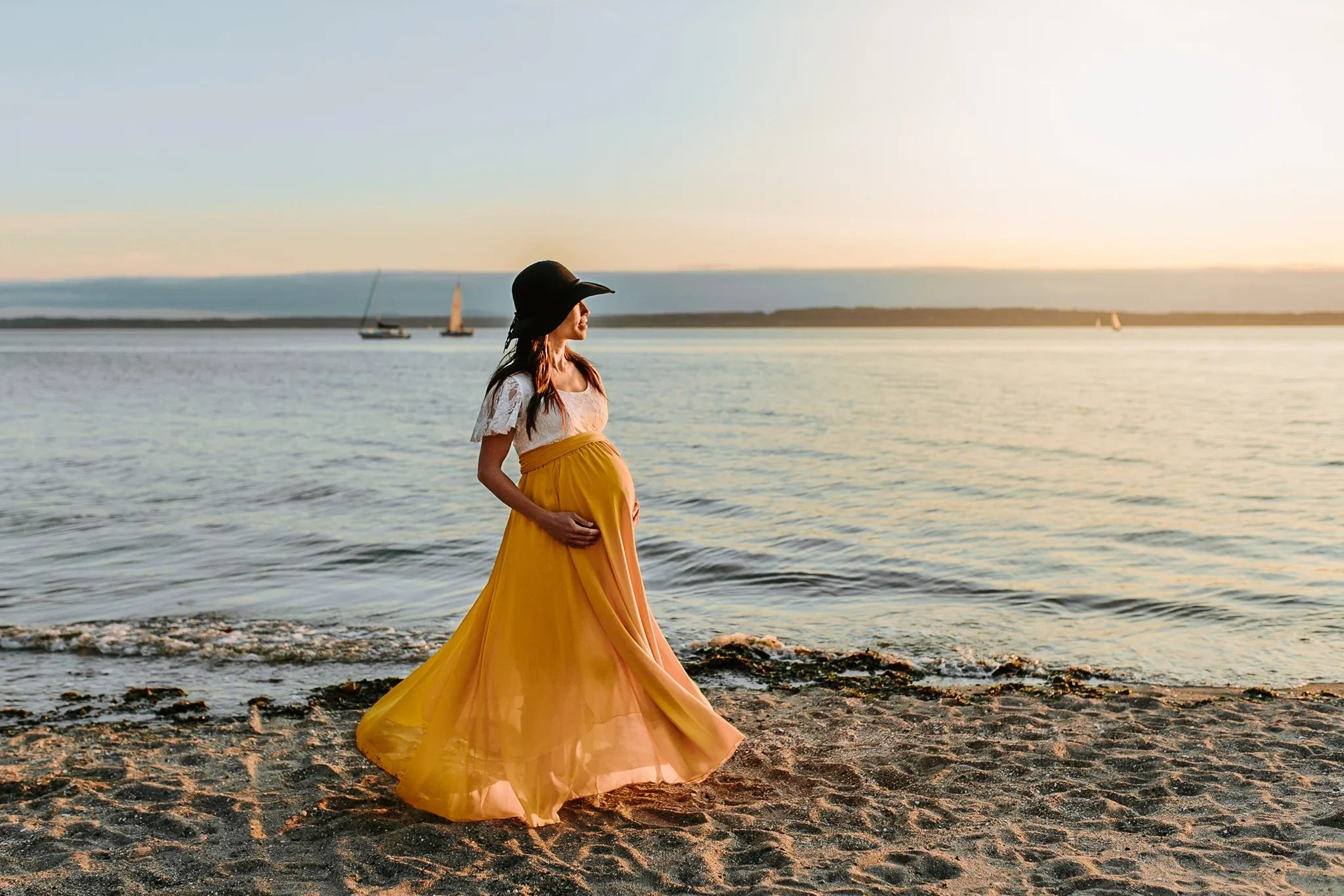 Woman in a flowing yellow skirt stands at the water’s edge at sunset