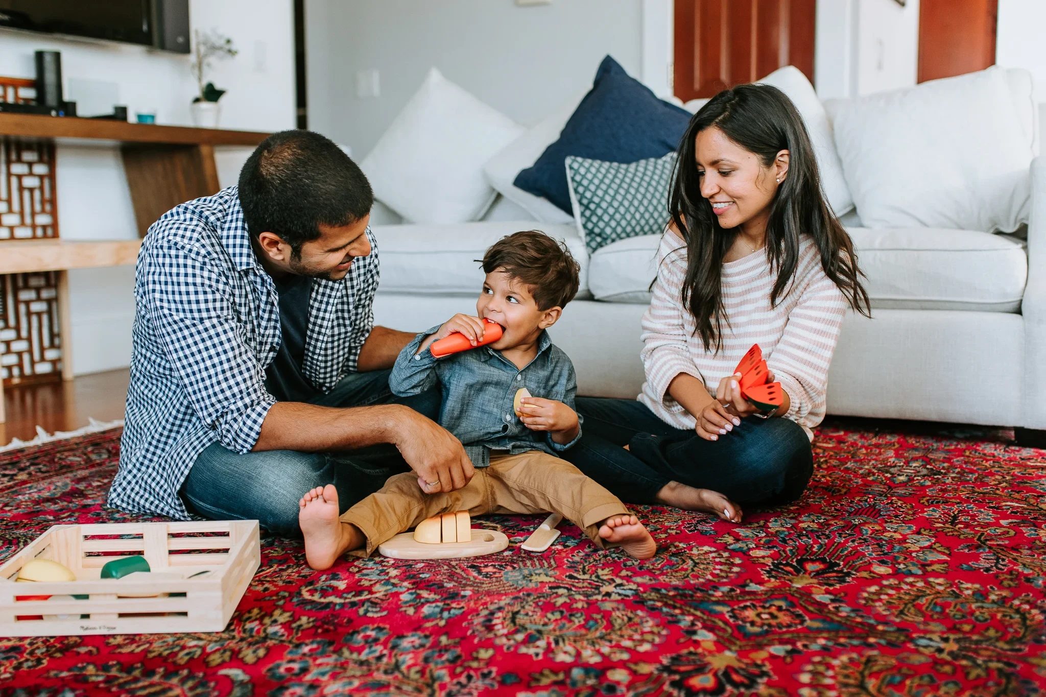 Two adults and a child play with toys on a patterned rug