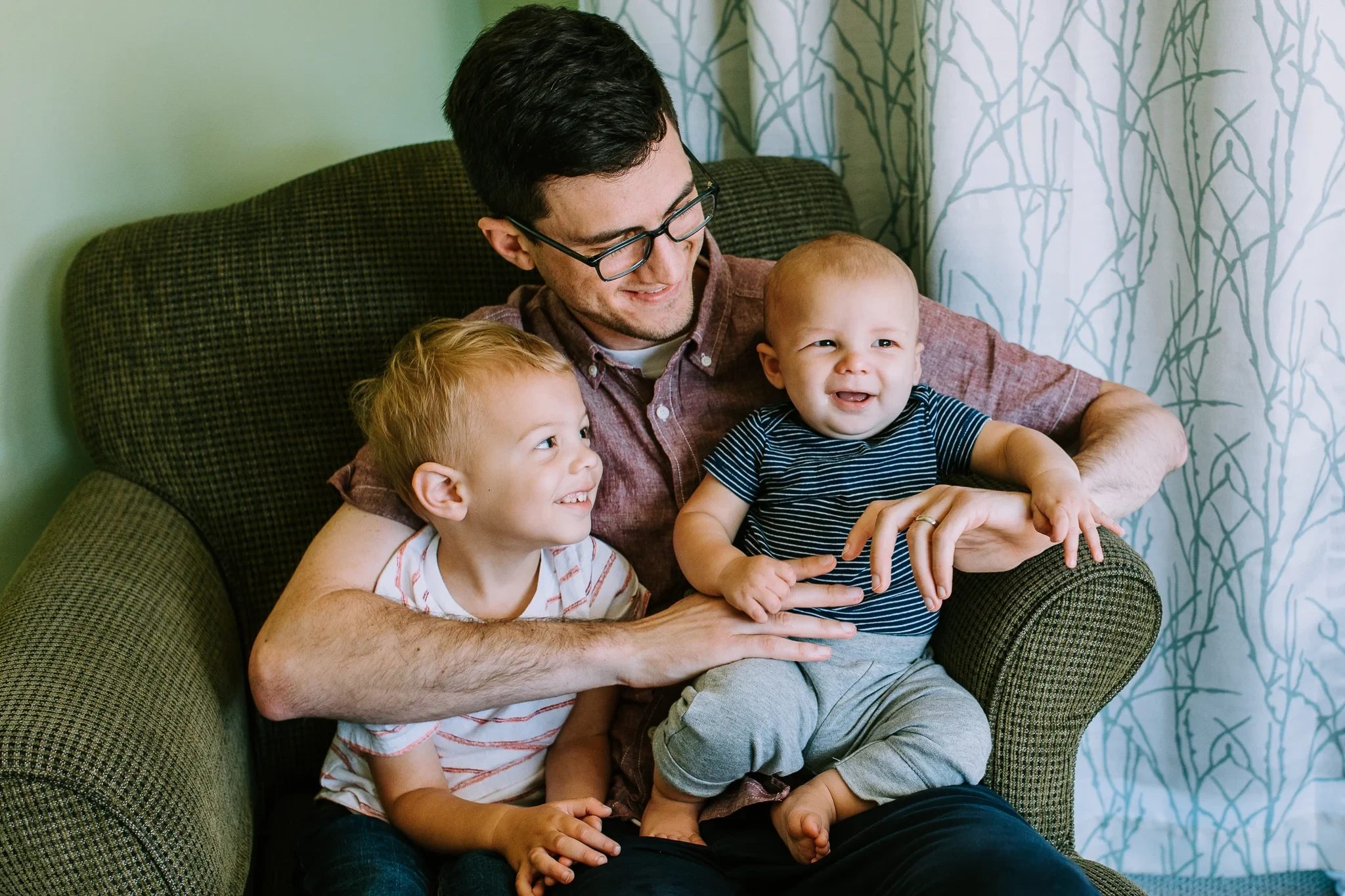 Man in glasses holds two smiling children in an armchair
