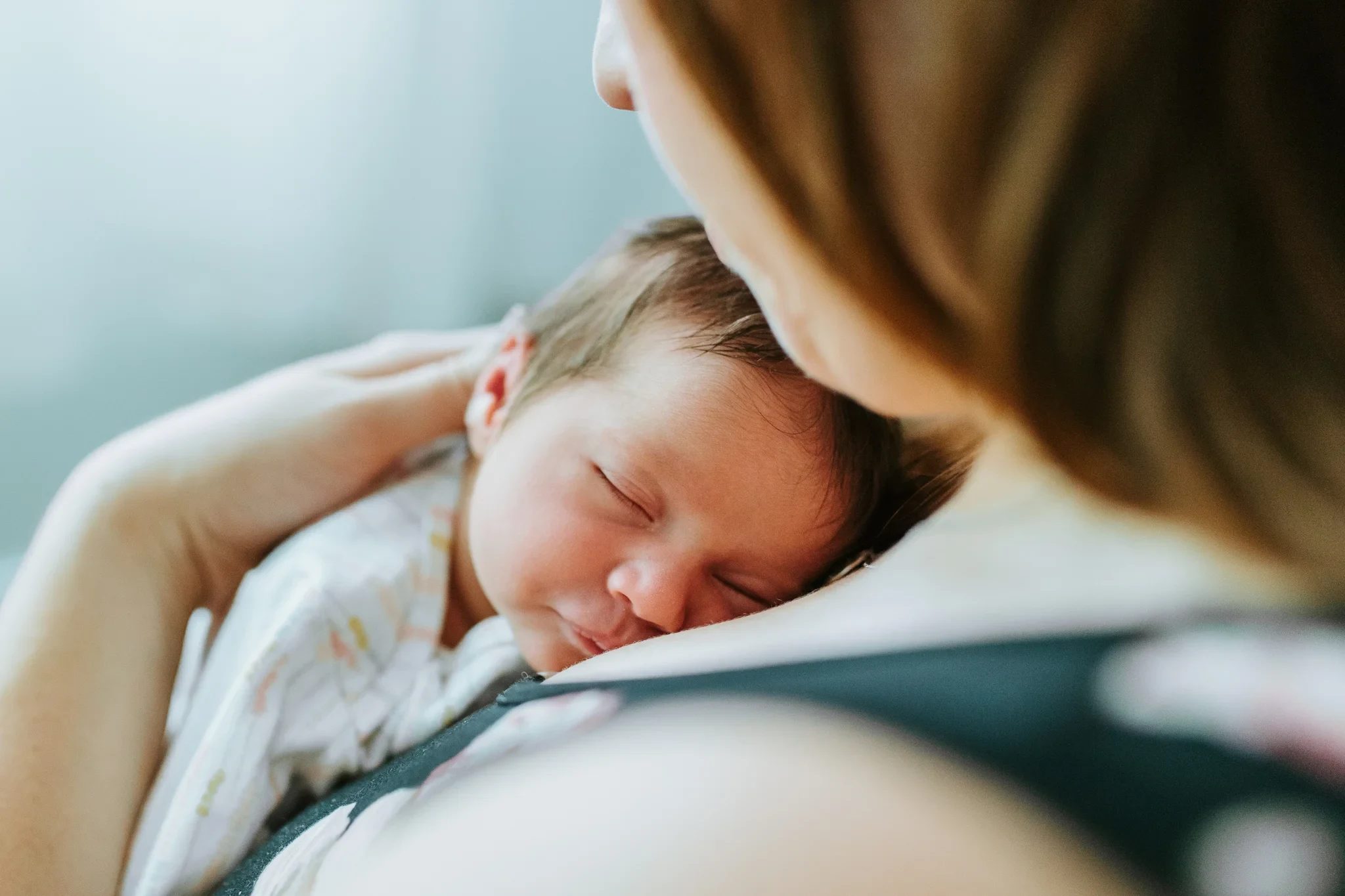 Baby sleeps against a woman’s shoulder in a soft carrier