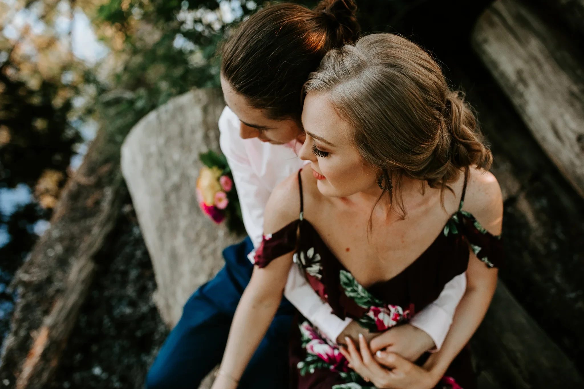 Two adults lean together beside a tree in dappled sunlight