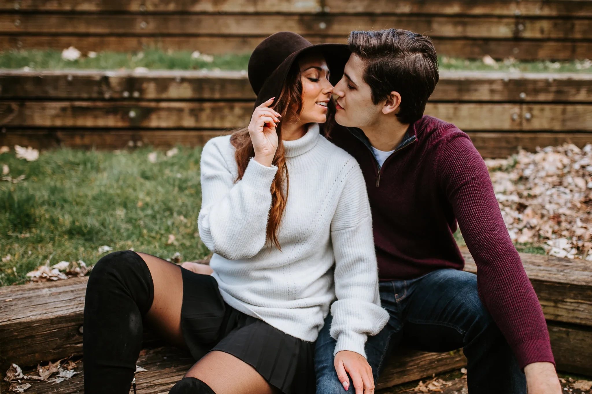 Two adults sit close together on a bench beneath wooden steps