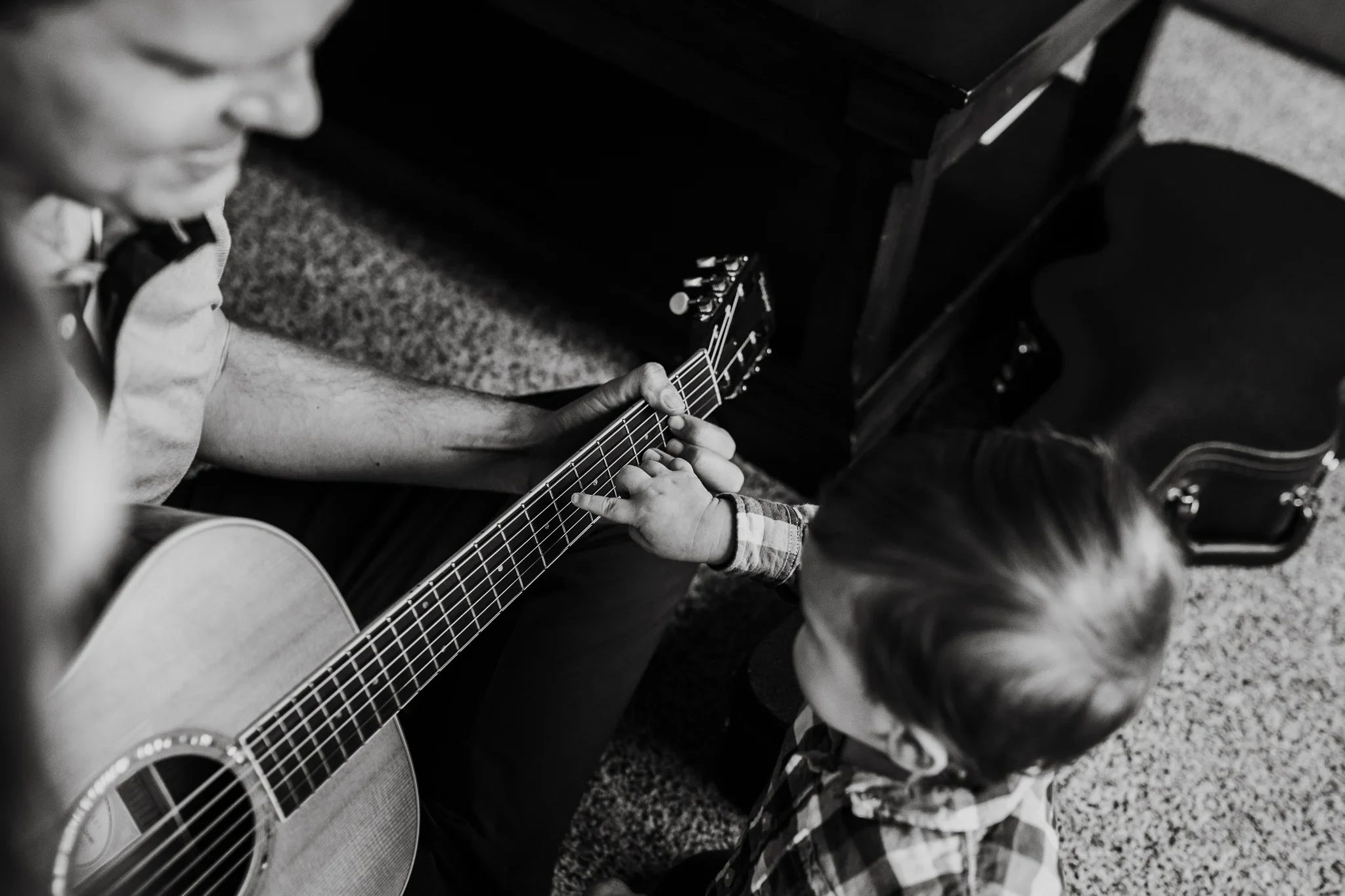 Black-and-white close-up of a child reaching toward guitar strings