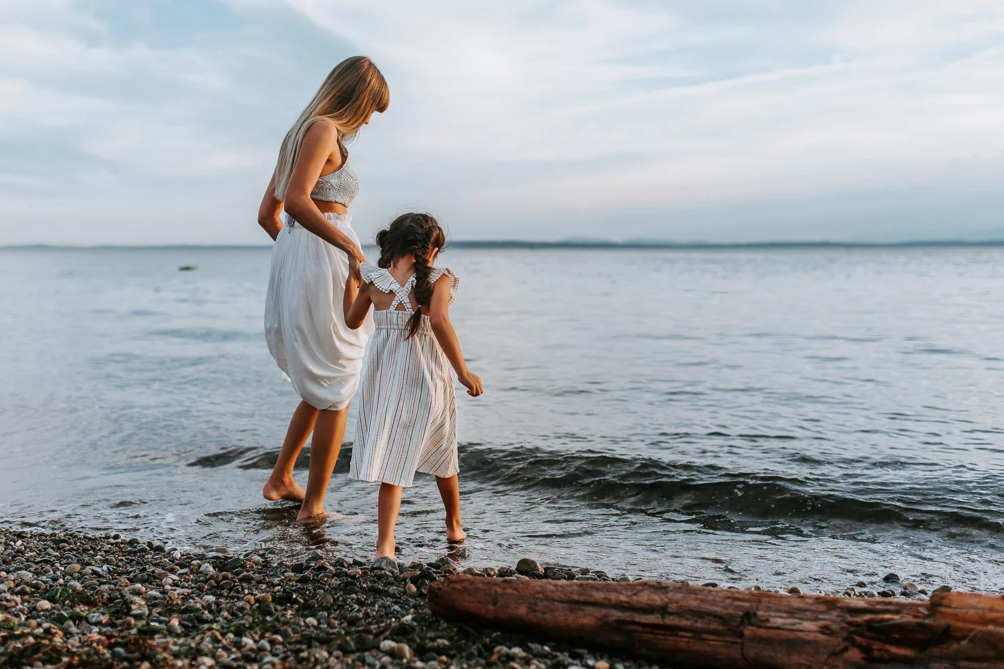 Woman and child balance on a log at the water’s edge