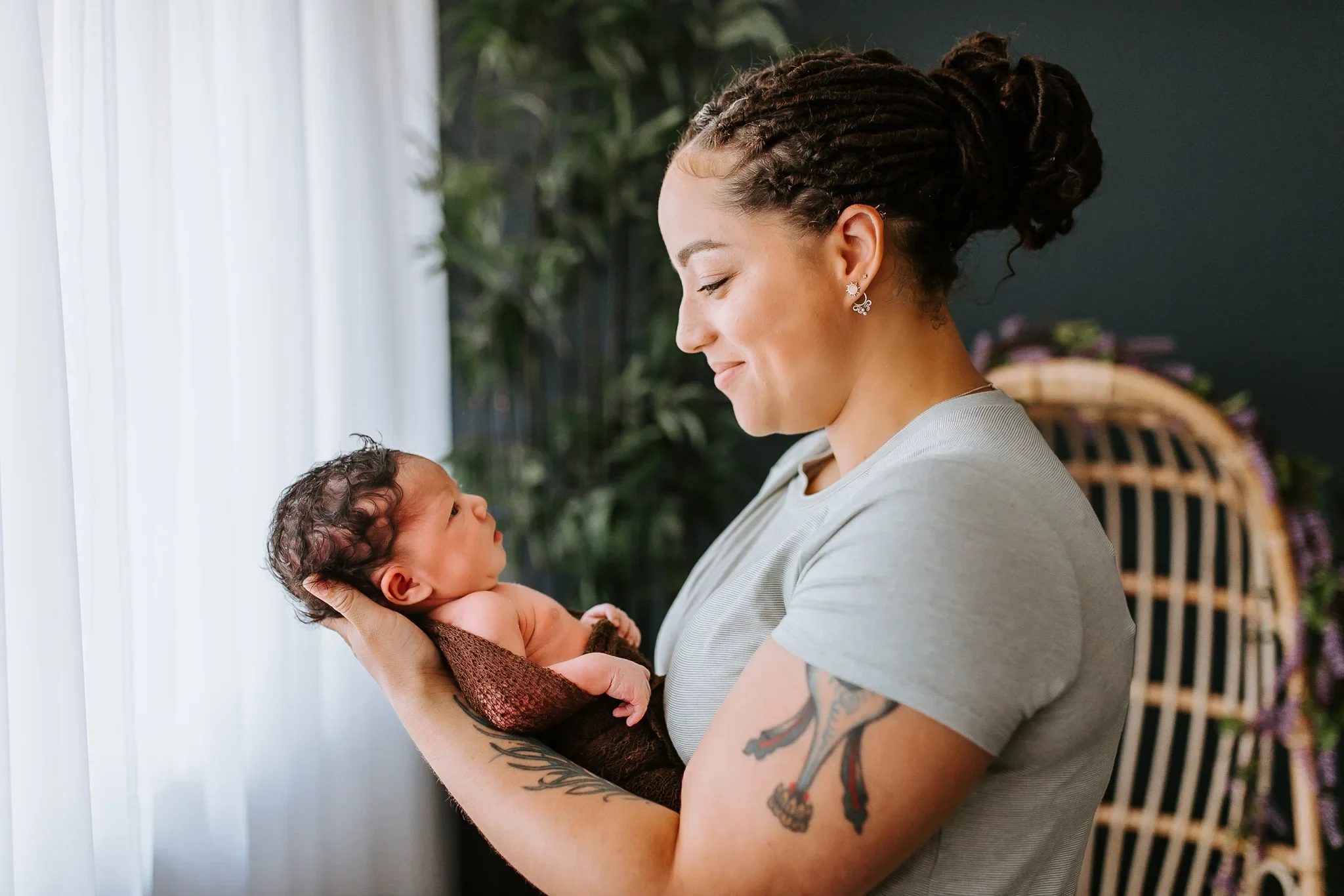 Woman holds a small baby in both hands beside a window
