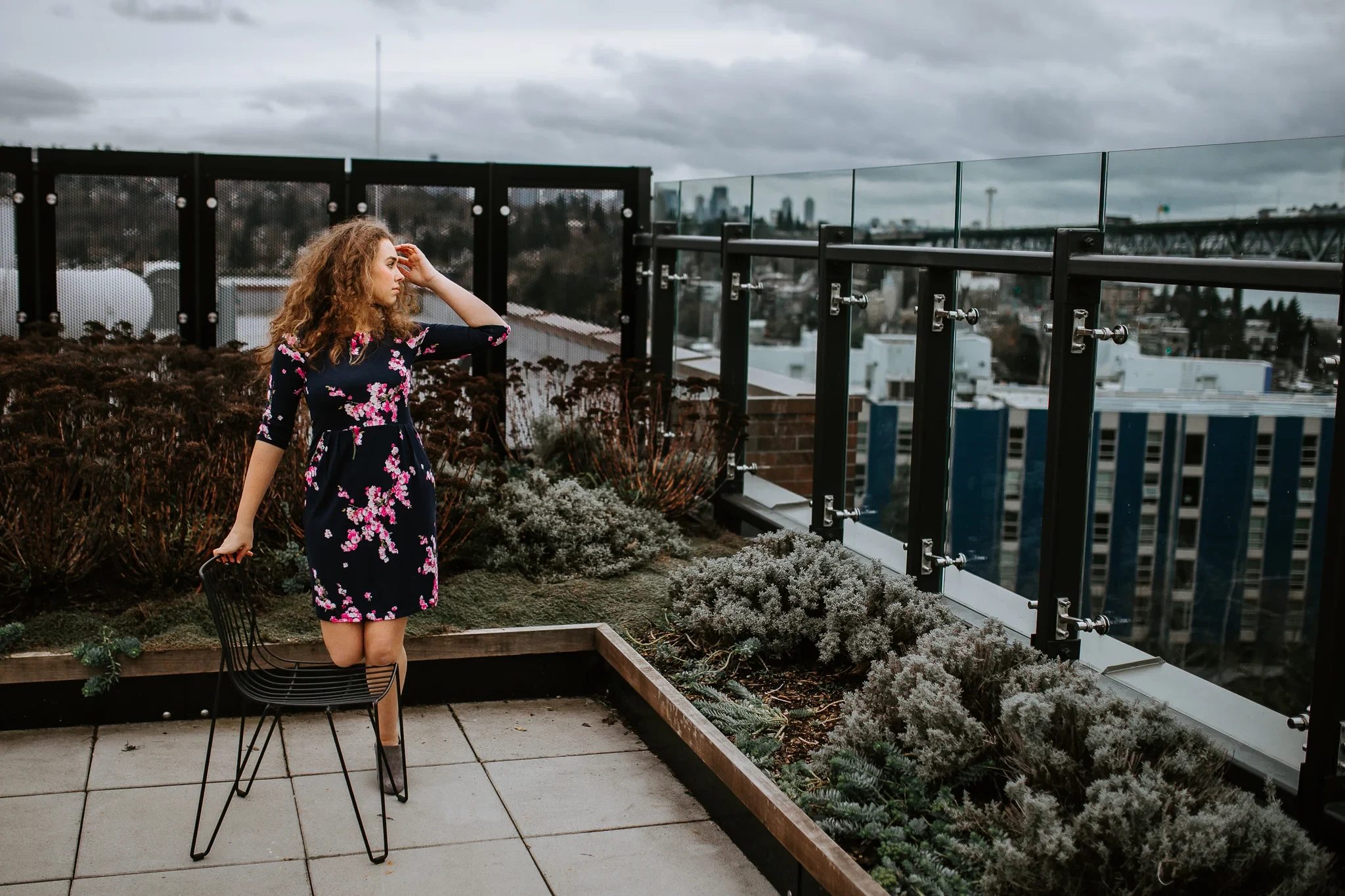Woman in a floral dress stands beside a chair on a rooftop garden