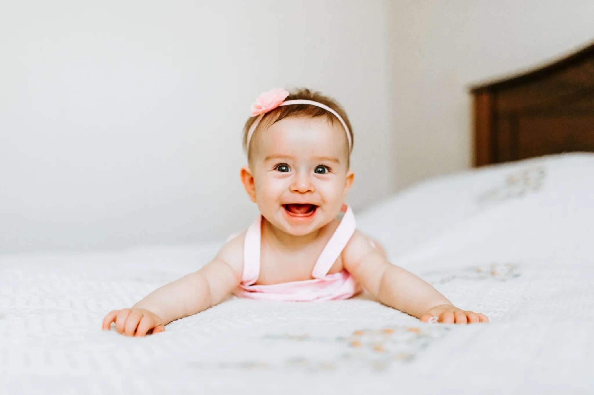 Smiling baby in pink lifts their head above white bedding