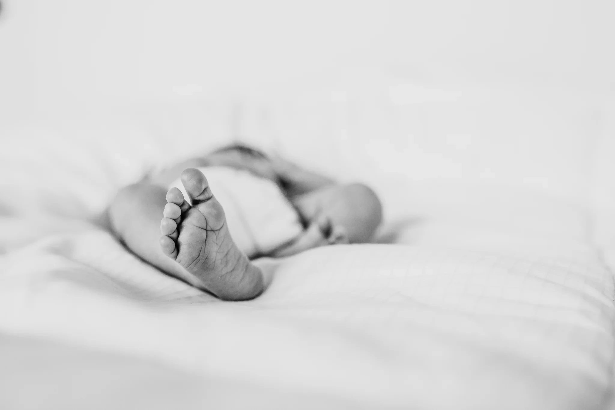 Black-and-white close-up of a baby’s feet on soft bedding