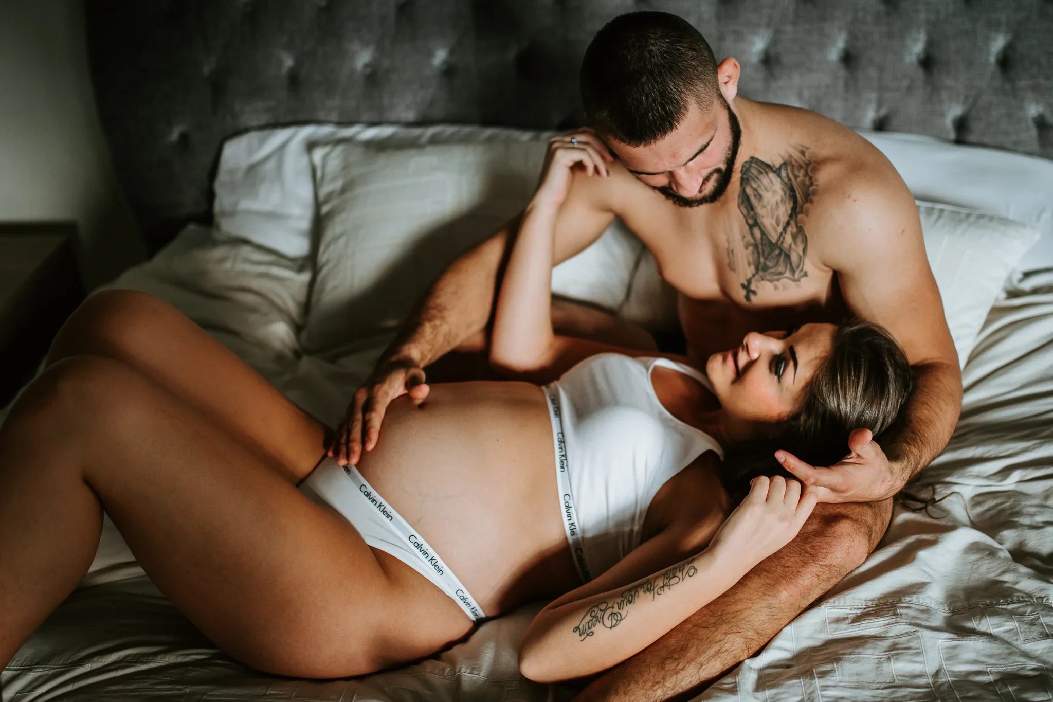 Two adults gaze at one another while reclining on a bed