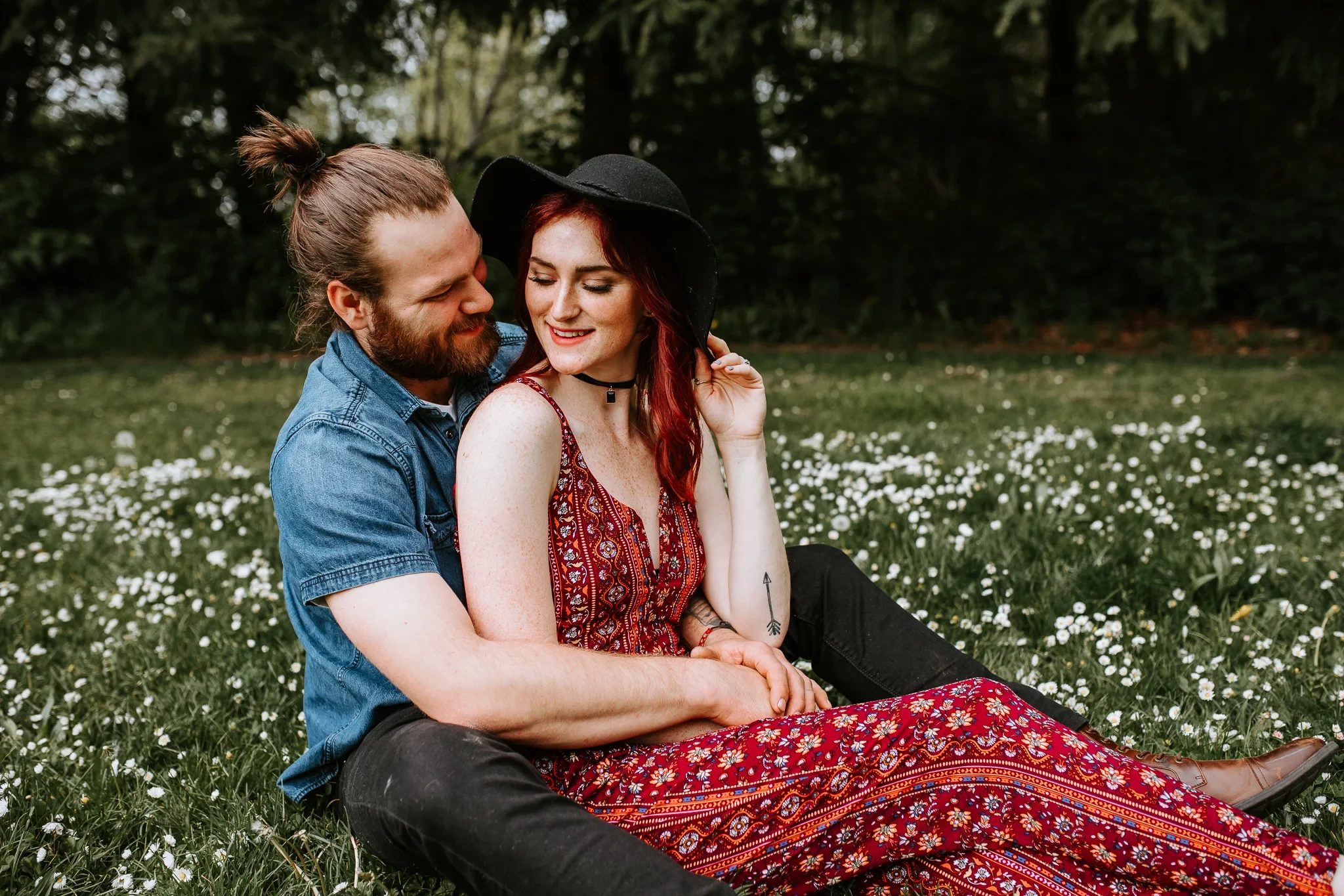 Two adults sit close together beside a meadow of small white flowers