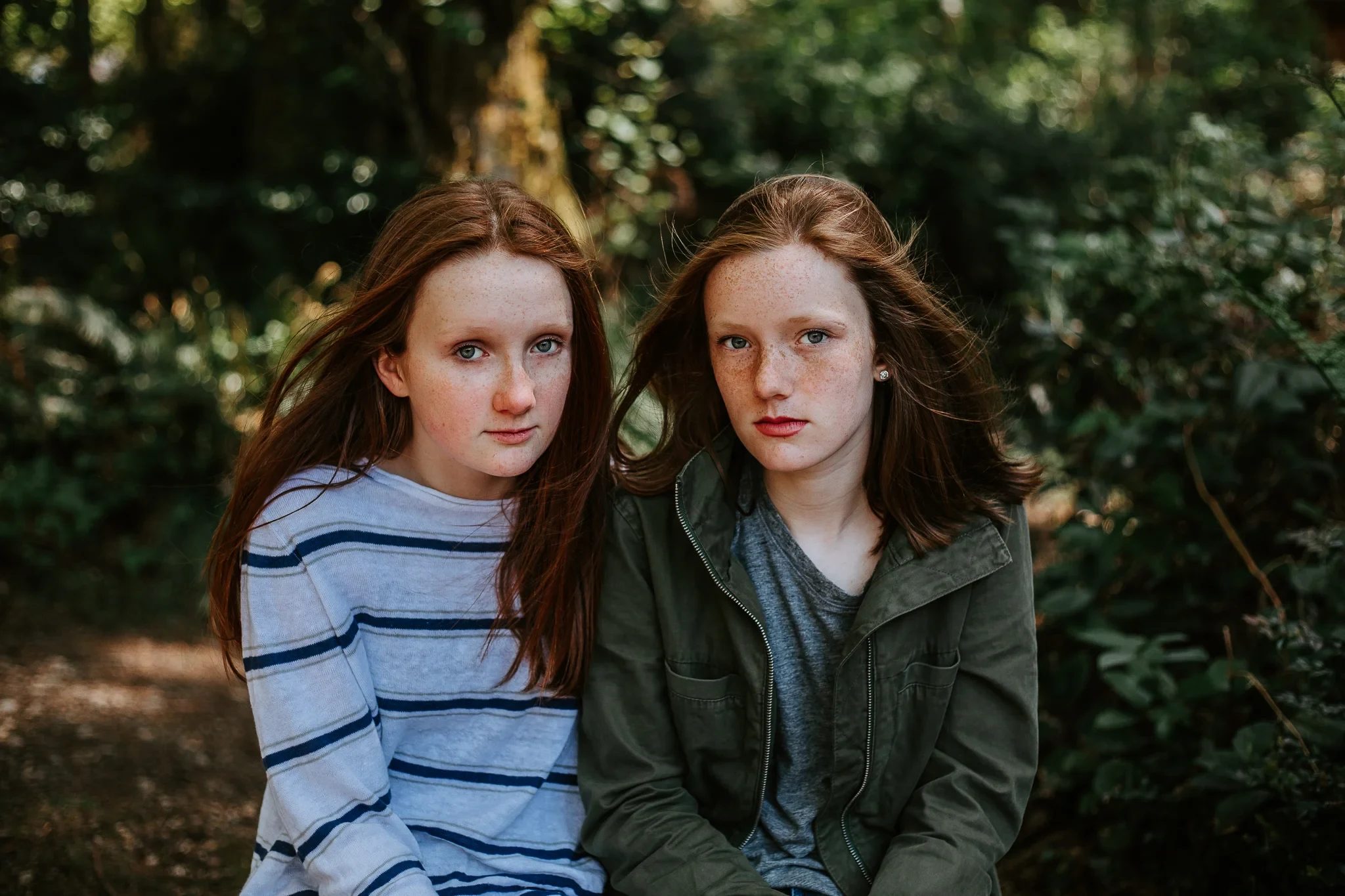 Two young people sit shoulder to shoulder against a leafy background