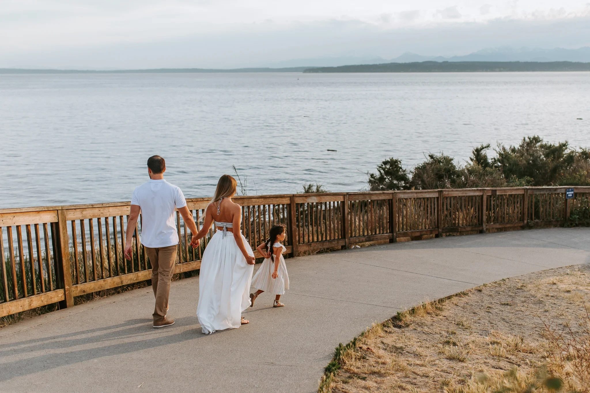 Family walks away along a waterfront path beside a wooden fence