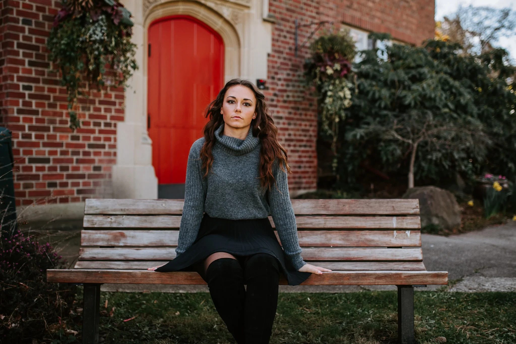 Woman in a grey sweater sits on a bench in front of a red door