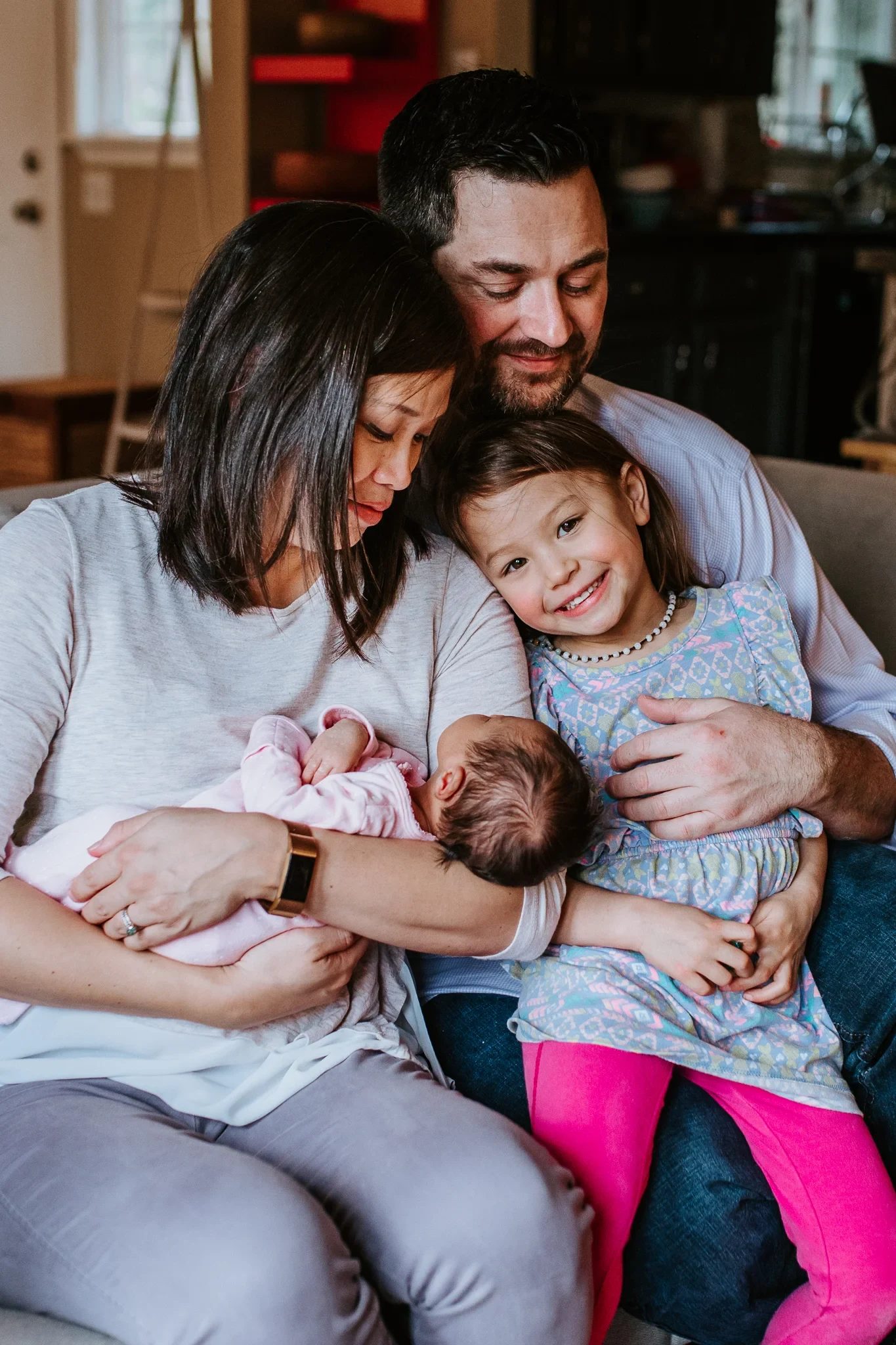 Family sits together holding a baby on a sofa